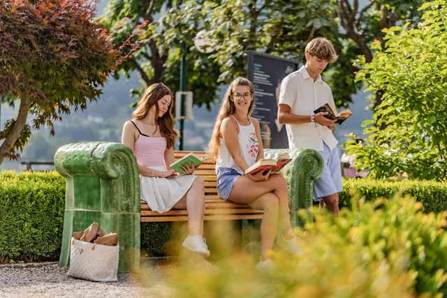 Drei Schüler:innen lesen auf einer Parkbank mit Armlehnen aus Gmundner Keramik, umgeben von Grün.