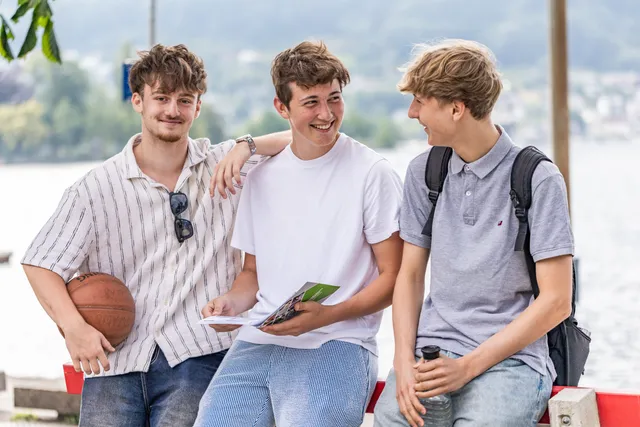Drei Schüler stehen lachend an der Seepromenade, einer hält einen Basketball, einer einen Schulfolder.