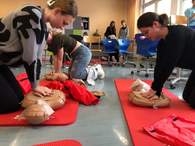 Zwei Schülerinnen üben im Klassenraum die Herzdruckmassage an Übungspuppen auf roten Matten.