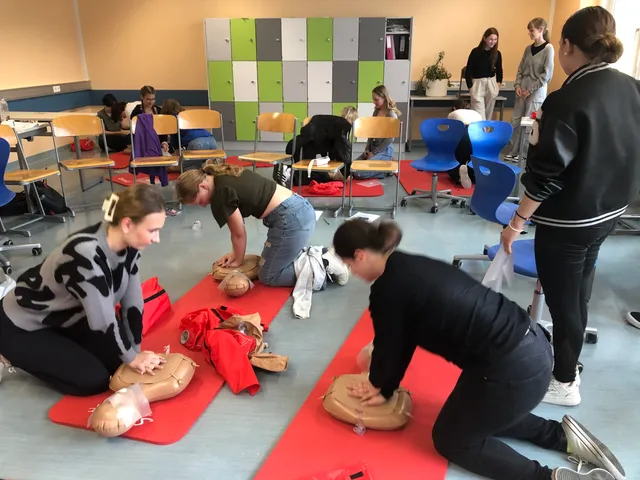 Mehrere Schüler:innen üben gleichzeitig die Herzdruckmassage an Übungspuppen; im Hintergrund bunte Spinde.