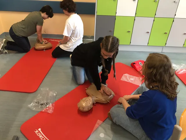 Schüler:innen knien auf Matten und üben die Herzdruckmassage, eine Mitschülerin sieht zu.