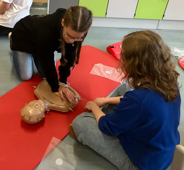 Nahaufnahme: Eine Schülerin drückt mit beiden Händen auf den Brustkorb einer Übungspuppe.