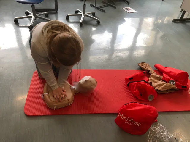 Eine Schülerin übt die Herzdruckmassage; daneben liegen die roten Taschen der Übungspuppen.