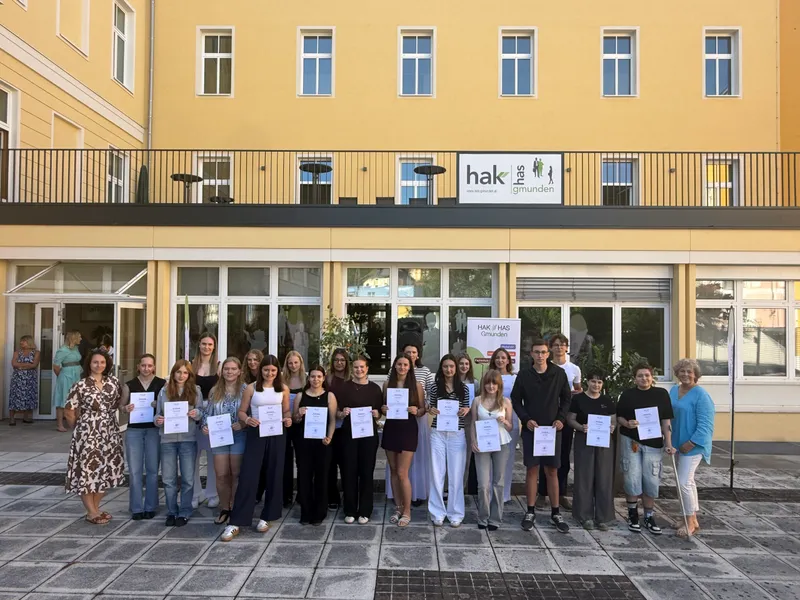 Rund zwanzig Schülerinnen und Schüler der HAK-Guides stehen mit ihren Zertifikaten in der Hand vor dem Eingang der HAK/HAS Gmunden, begleitet von zwei Lehrerinnen.
