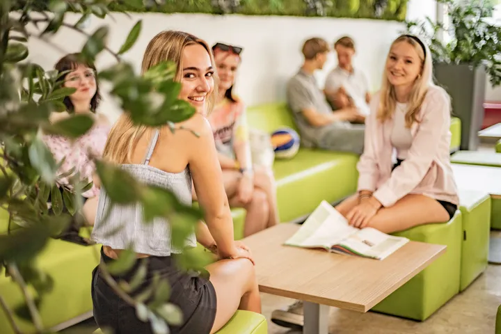 Schülerinnen und Schüler entspannen im begrünten Loungebereich der HAK Gmunden und blättern in einer Zeitschrift.