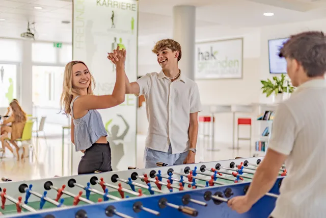 Zwei Schüler:innen klatschen am Wuzzeltisch in der Aula ab, ein dritter spielt weiter.